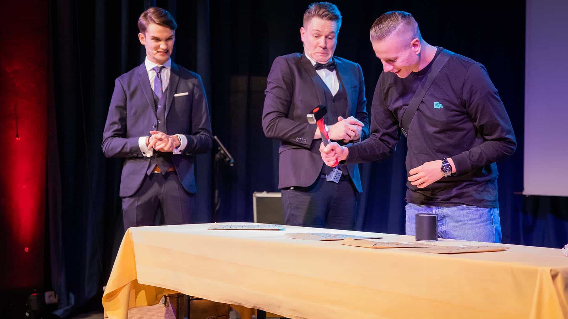 Ein Mann schlägt mit einem Hammer auf den Tisch, Thomas und Vincent erschrecken