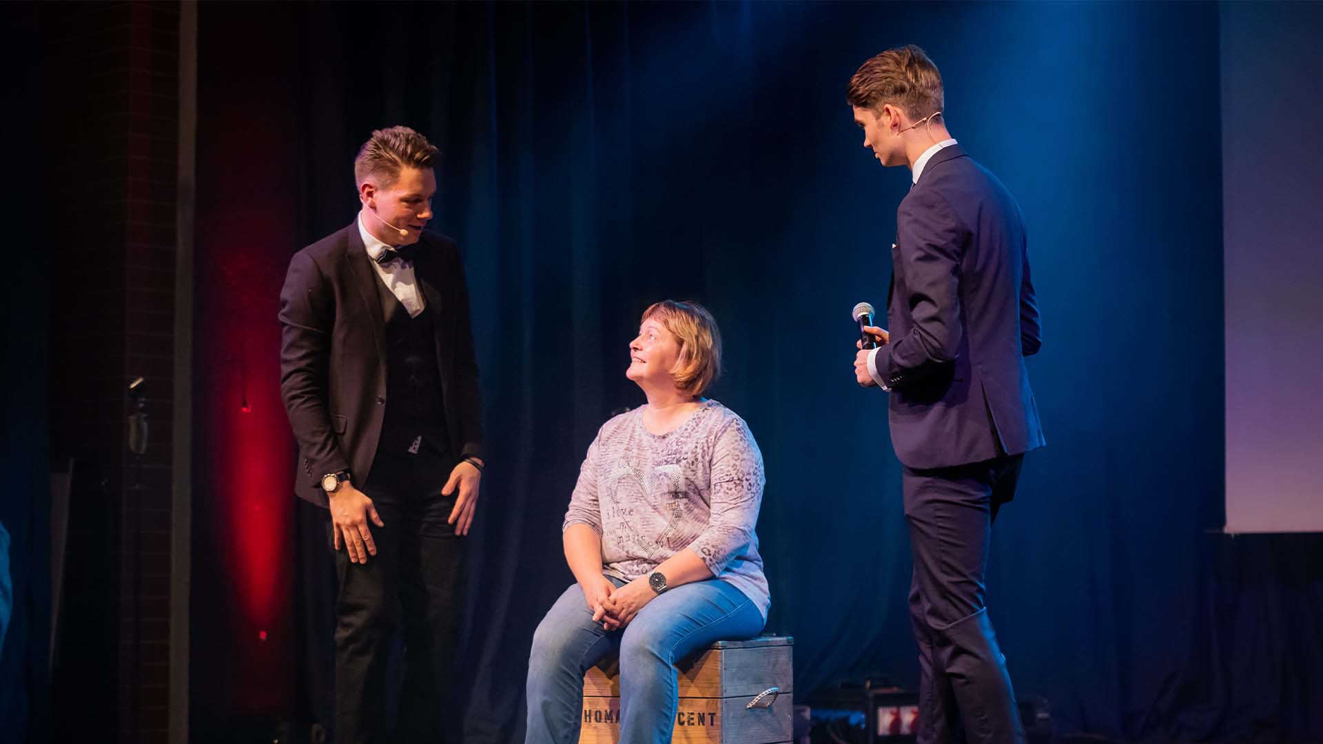 Eine Zuschauerin sitzt auf einer Kiste, Thomas Majka und Vincent Frommer erklären ihr etwas