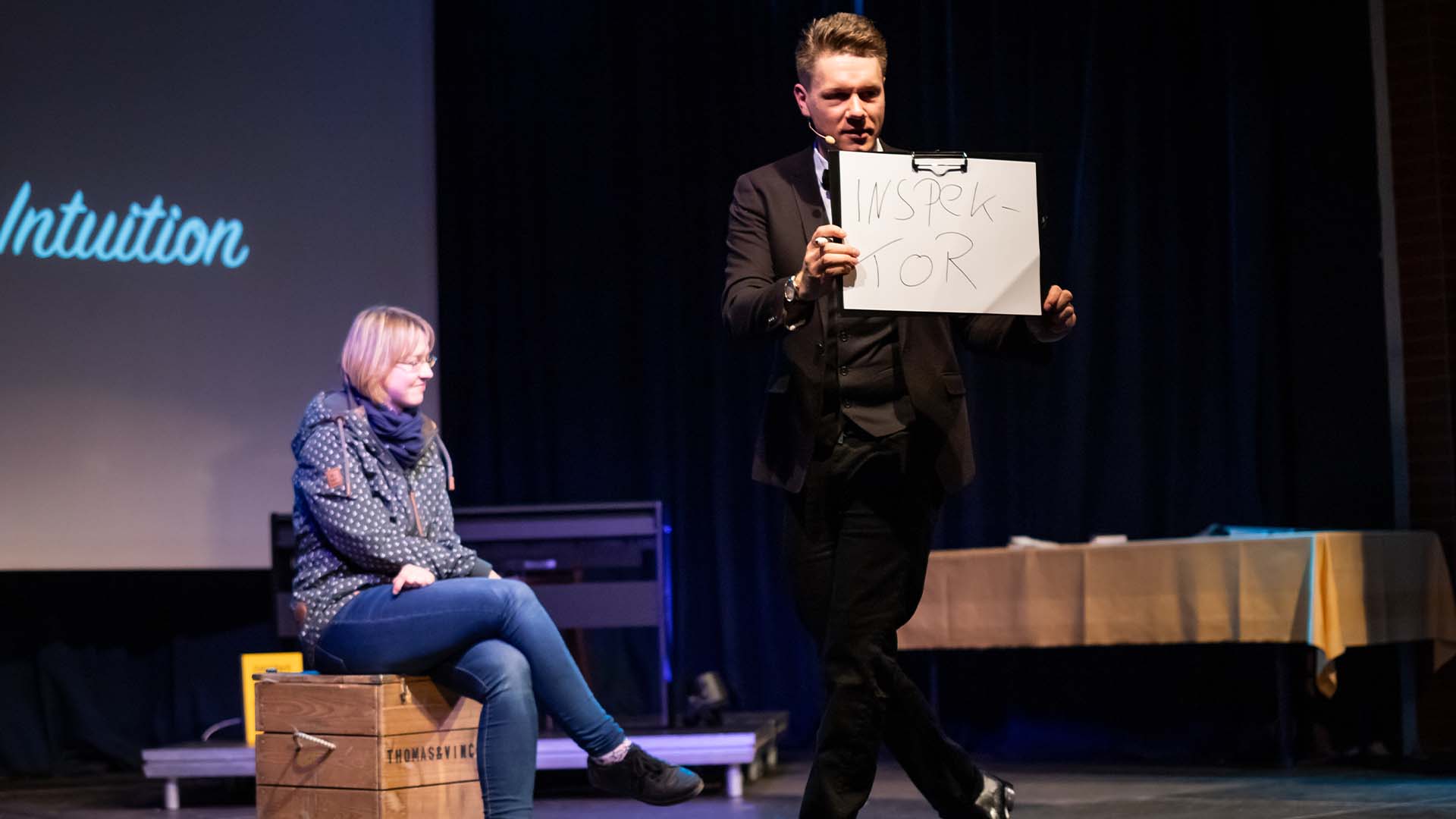 Thomas hält einen Block mit Vorhersage, im Hintergrund sitzt eine Zuschauerin