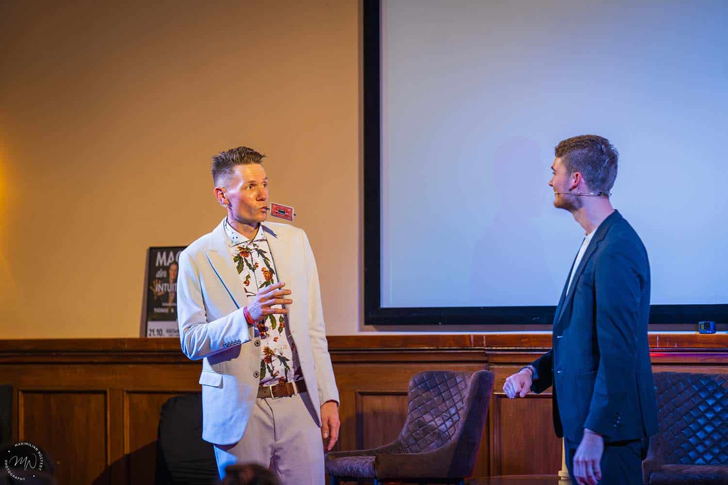 Thomas hat einen Löffel mit Karte im Mund, während Vincent ihm etwas erklärt.