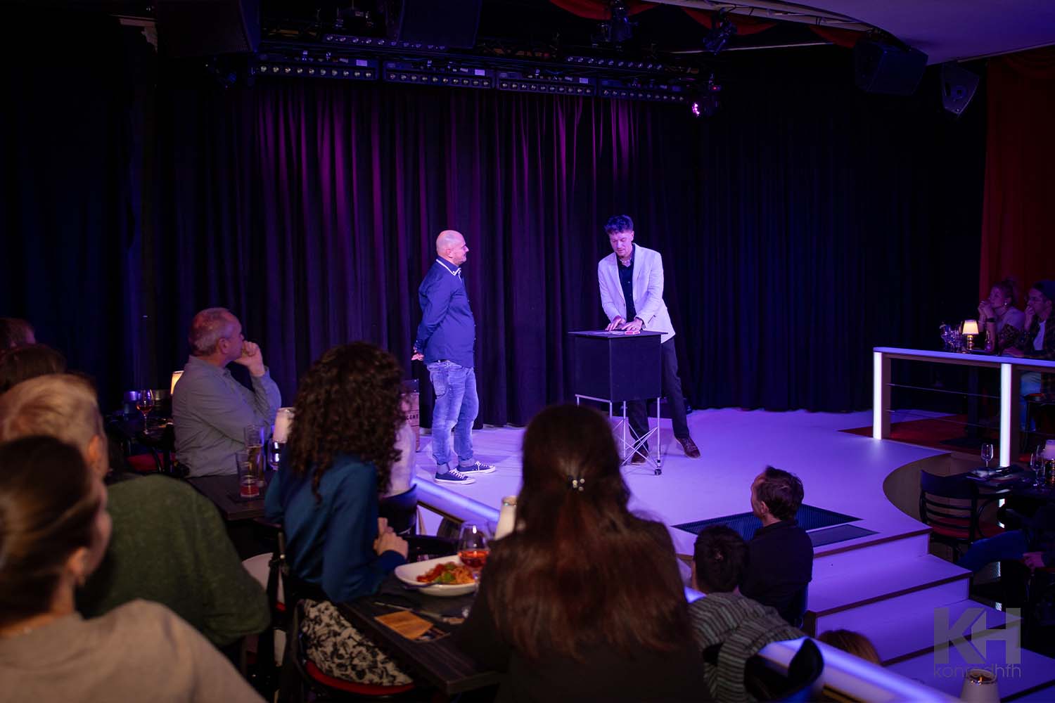 Thomas Majka steht mit einem Zuschauer an einem Tisch, das Publikum ist im Hintergrund sichtbar