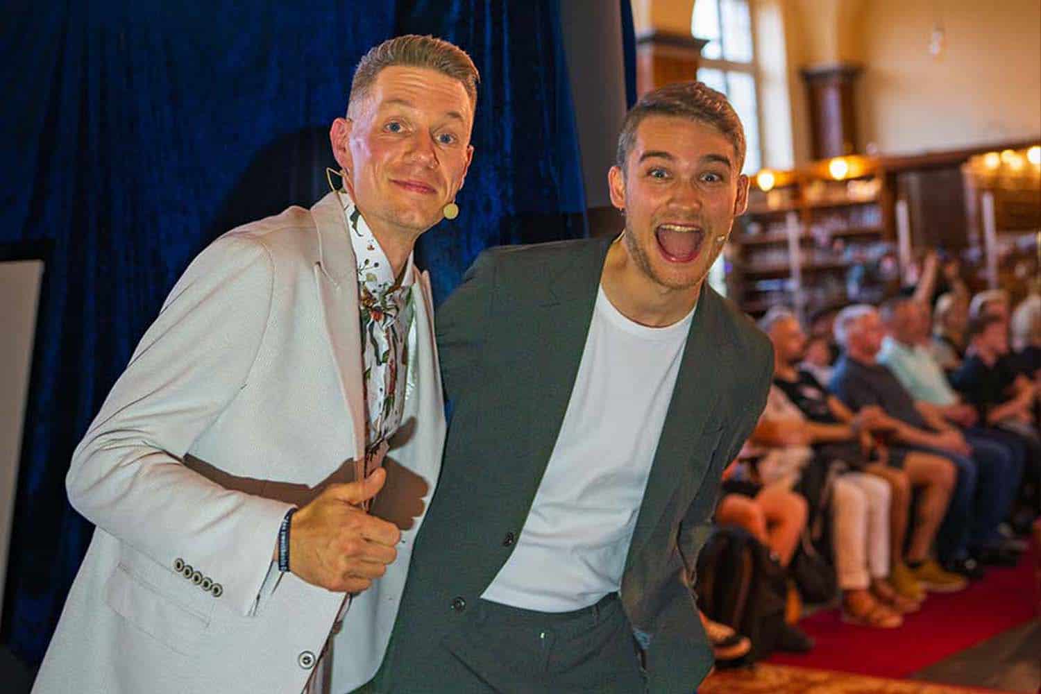 Thomas Majka und Vincent Frommer schauen hinter der Bühne hervor auf das Publikum.