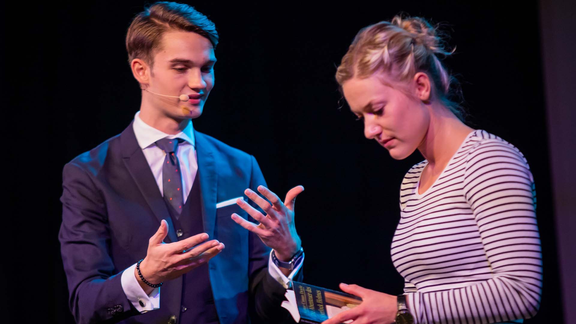 Vincent überreicht einer Zuschauerin ein Buch und erklärt etwas
