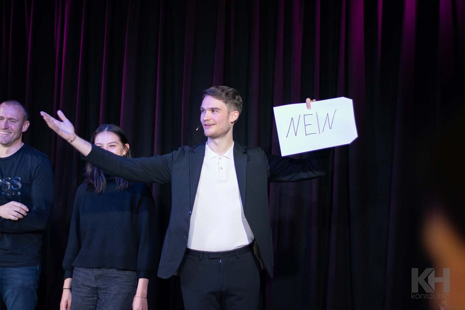 Vincent Frommer lacht ins Publikum und hält einen Briefumschlag mit der Aufschrift „Nein“