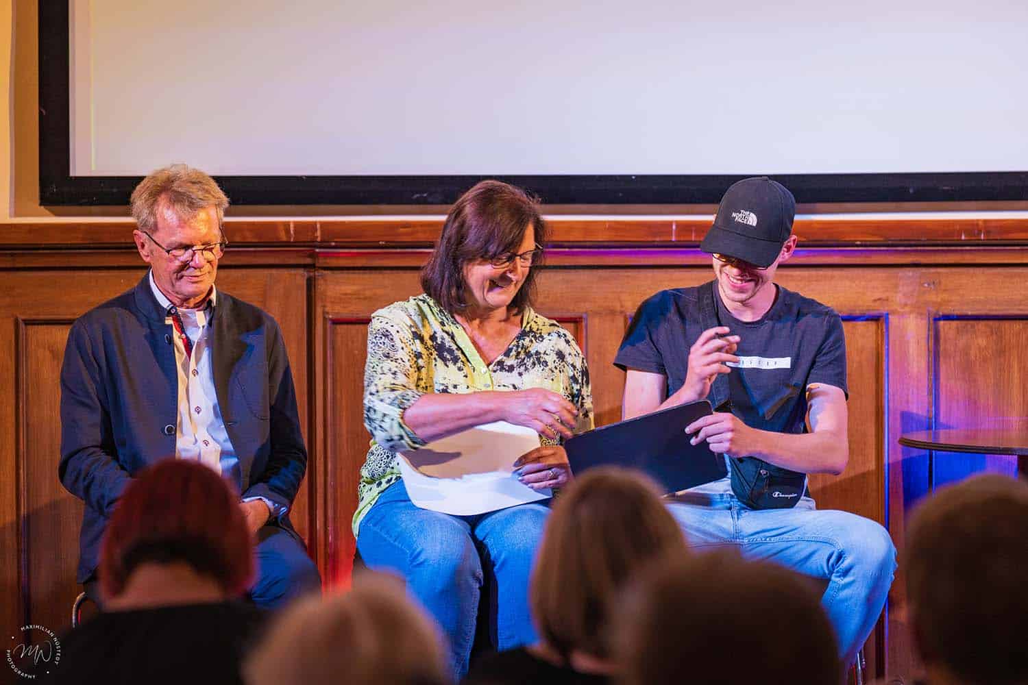 Drei Zuschauer schreiben etwas auf und lachen dabei.