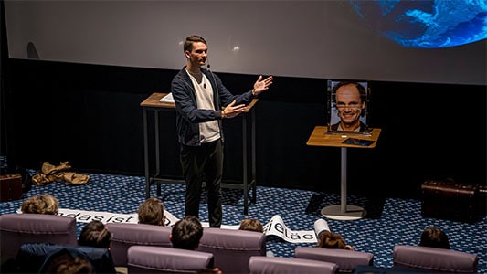 Vincent Frommer erklärt dem Publikum etwas, während auf der Leinwand ein Bild von Olaf Schubert zu sehen ist bei der Mindtrix-Show in Bautzen