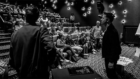 Schwarz-weiß-Aufnahme von Thomas Majka und Vincent Frommer von hinten mit Blick auf das Publikum der Mindtrix-Premiere in Bautzen