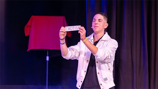 Merlin hält ein Klebeband mit dem Wort Emotion in der Hand während der Show im Carte Blanche Petit Theater Dresden