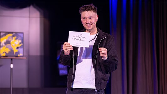 Thomas Majka hält eine von einem Gast gezeichnete Karte mit einem Auto darauf während der Show im Carte Blanche Petit Theater Dresden