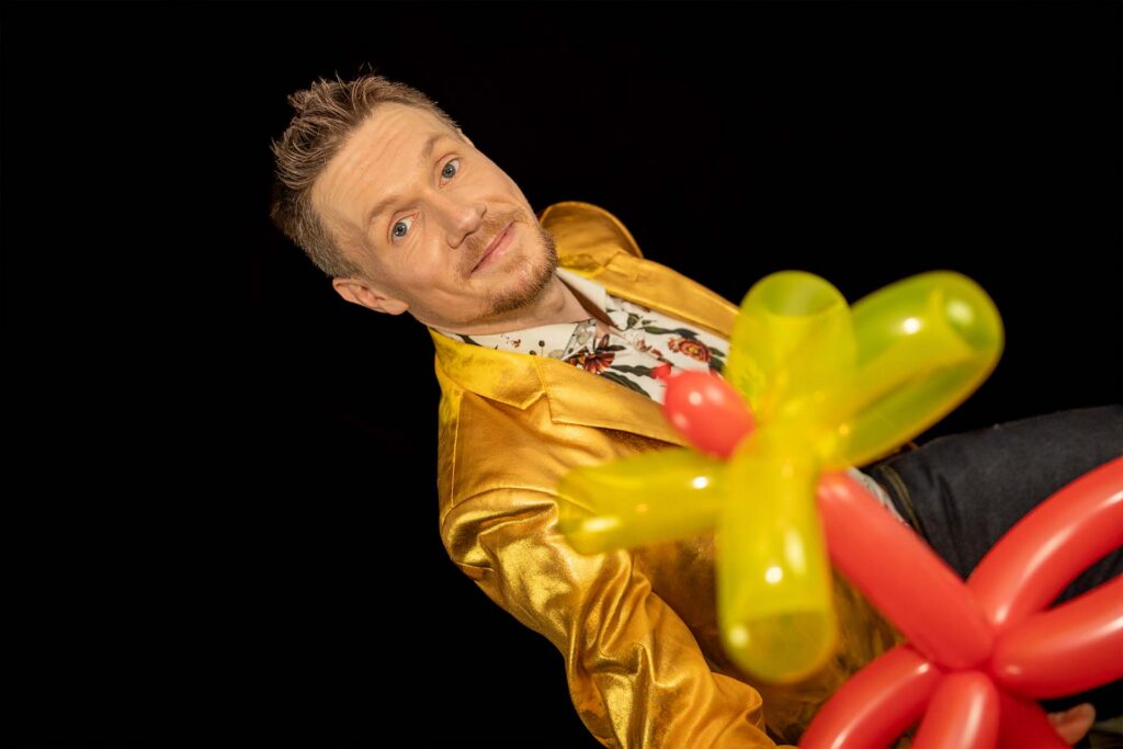 Kinderzauberer hält eine Ballonblume und begeistert Kinder auf einem Kindergeburtstag