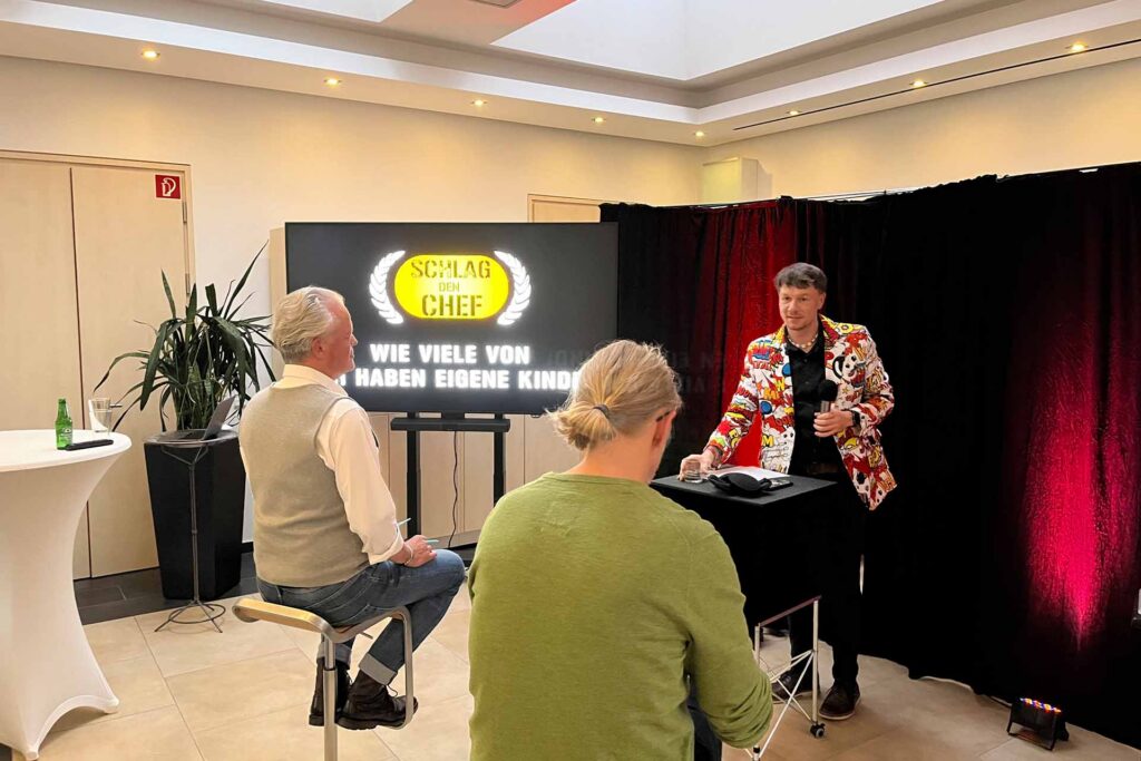 Quizshow Event Thomas Majka moderiert die Spielshow „Schlag den Chef“ bei einem Firmenevent, während zwei Teilnehmer gegeneinander antreten