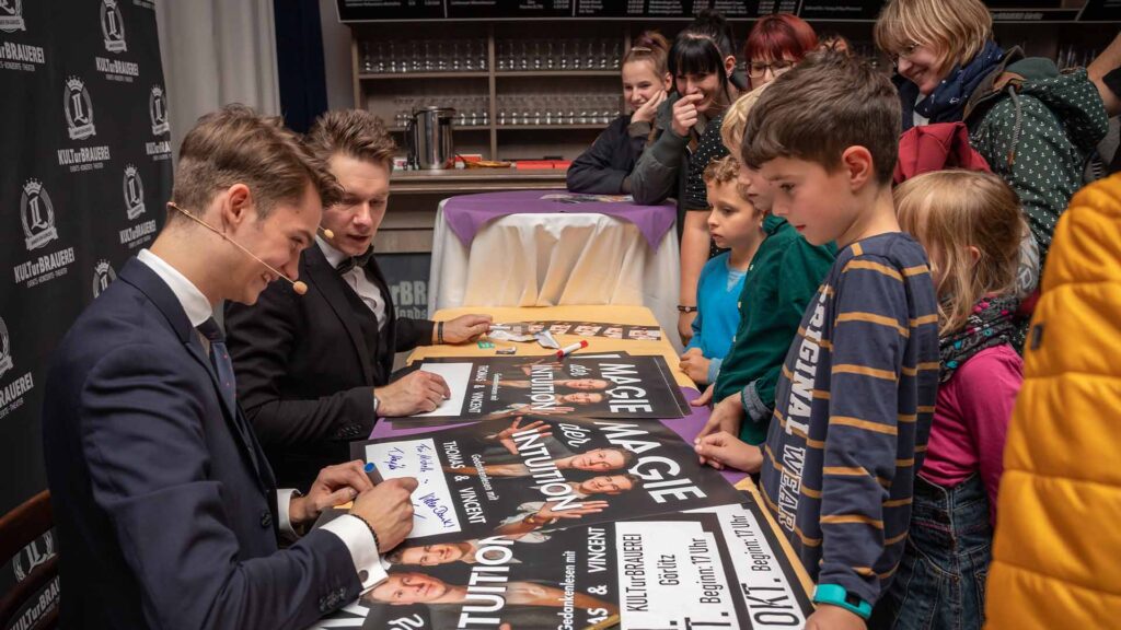 Thomas Majka und Vincent Frommer sitzen am Autogrammtisch und geben Autogramme nach einer Zaubershow