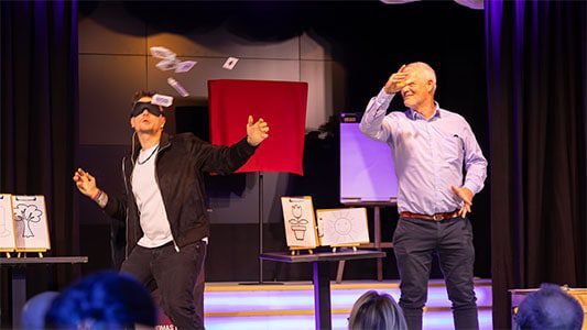 Ein Zuschauer wirft ein Kartenspiel in die Luft, während Thomas Majka mit verbundenen Augen auf der Bühne im Carte Blanche Petit Theater Dresden steht Mentalist Leipzig