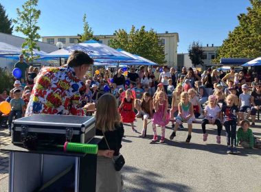 Kinderzauberer steht vor einer großen Kindergartengruppe und führt eine interaktive Zaubershow durch