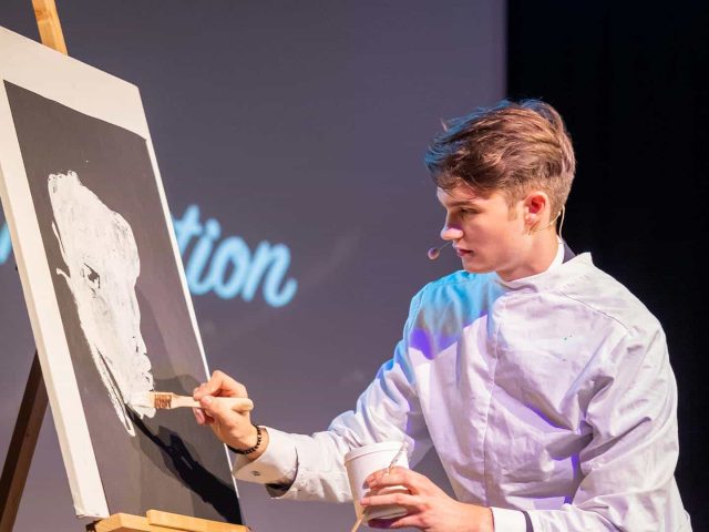 Vincent Frommer im weißen Kittel malt während der Show „Magie der Intuition“ auf eine Leinwand